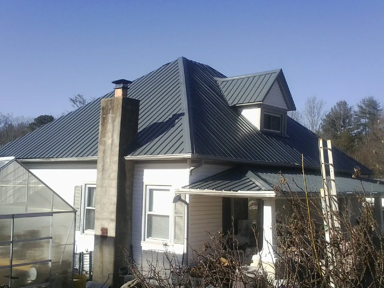 Dark blue standing seam metal roof on a white farmhouse with dormer — Slate & Tile Roof Repair by Roofing Brothers in Six Lakes