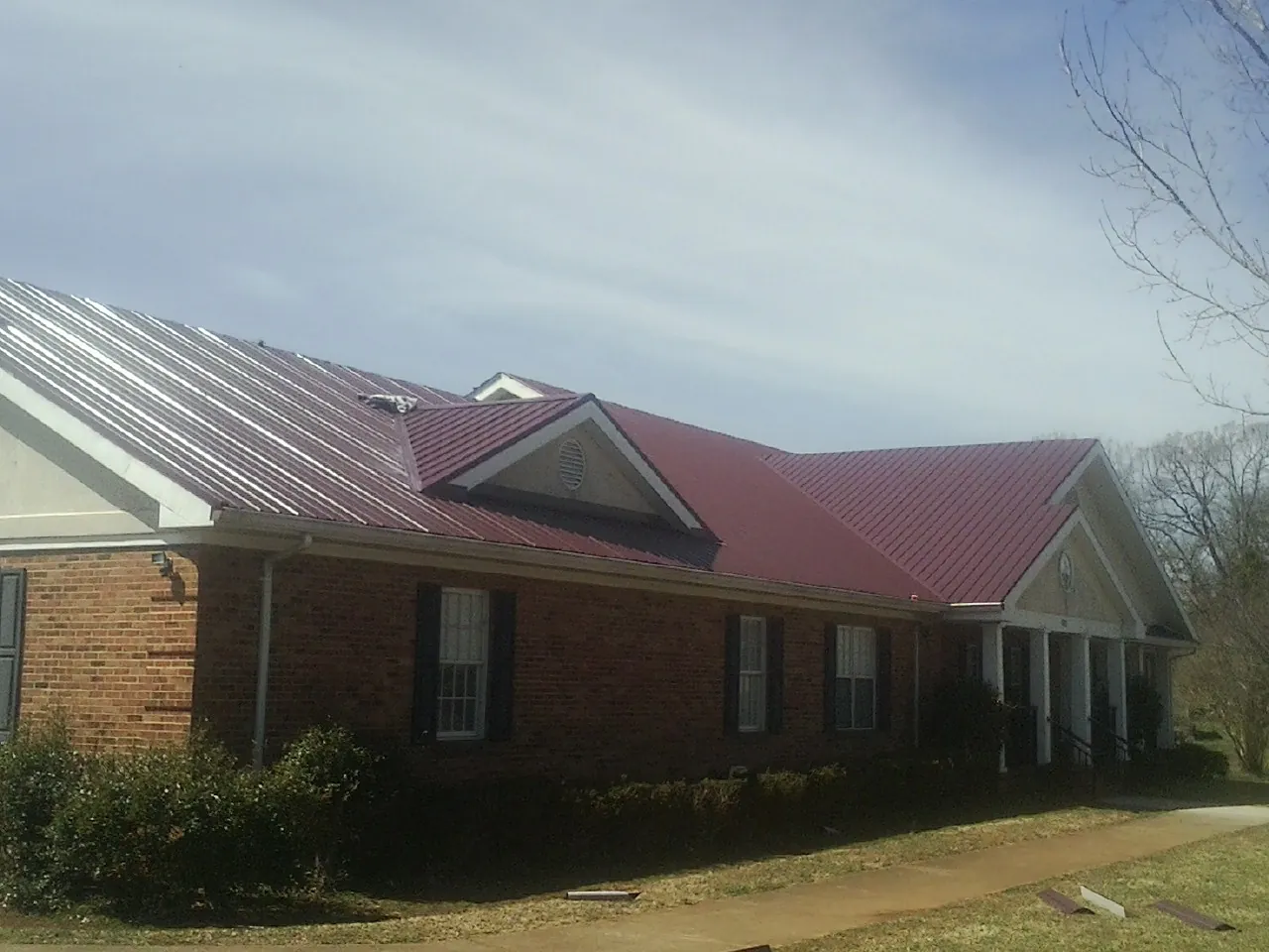 Red metal roof with gabled entries on a long brick building, from a Hail Damage Roof Repair job in Six Lakes