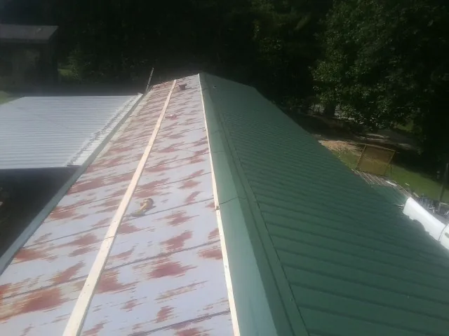 Old rusted panels beside newly installed green metal roofing — Wind Damage Roof Repair by Roofing Brothers in Six Lakes