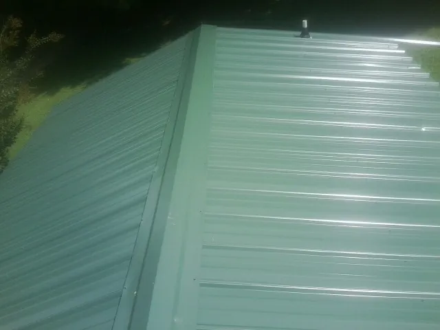 New green metal panels meeting at the ridge of a roof — Flat Roof Repair work by our crew in Six Lakes