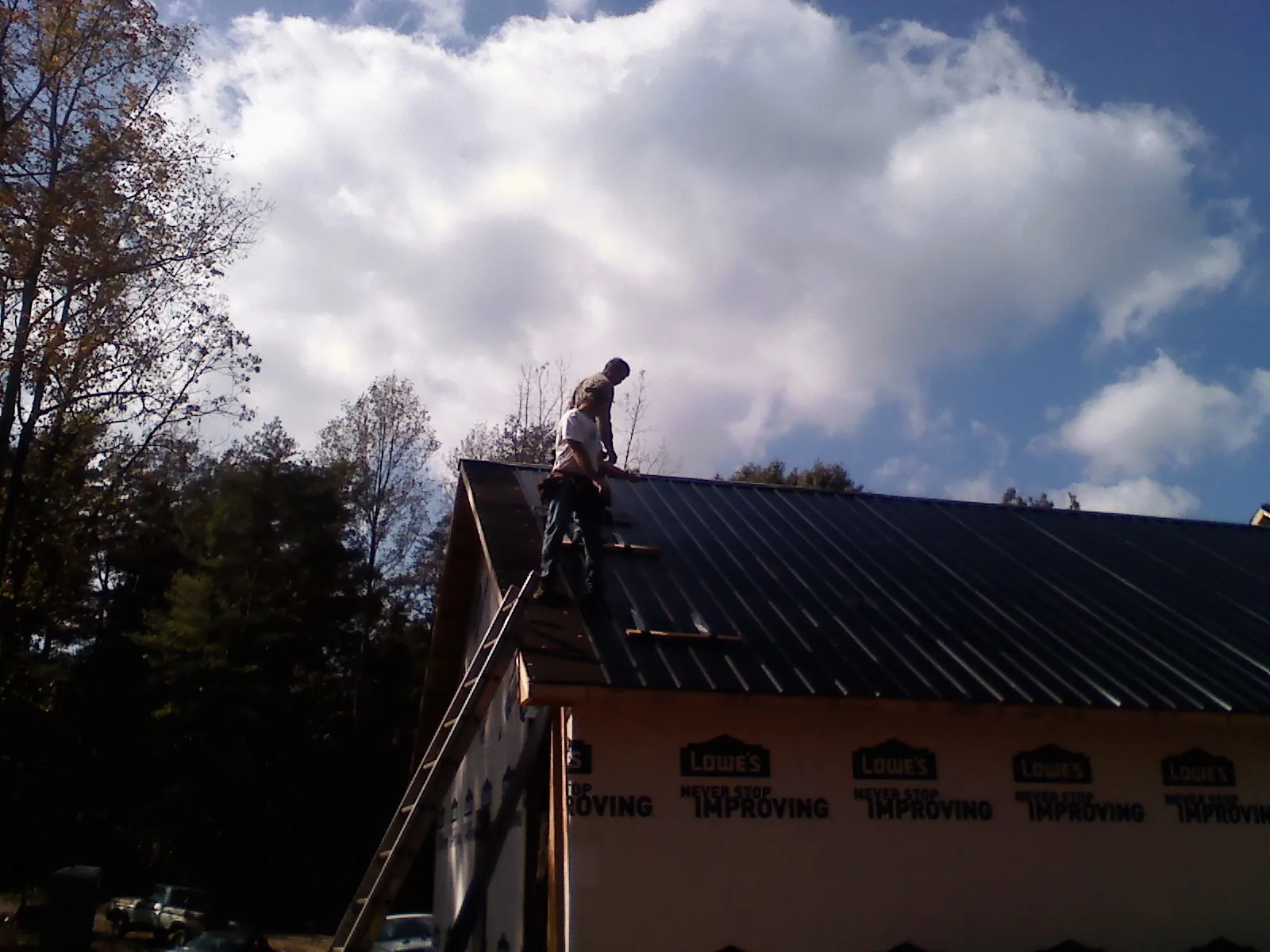 Roofer fastening dark metal panels high against a cloudy sky, from a Roof Inspection job in Six Lakes