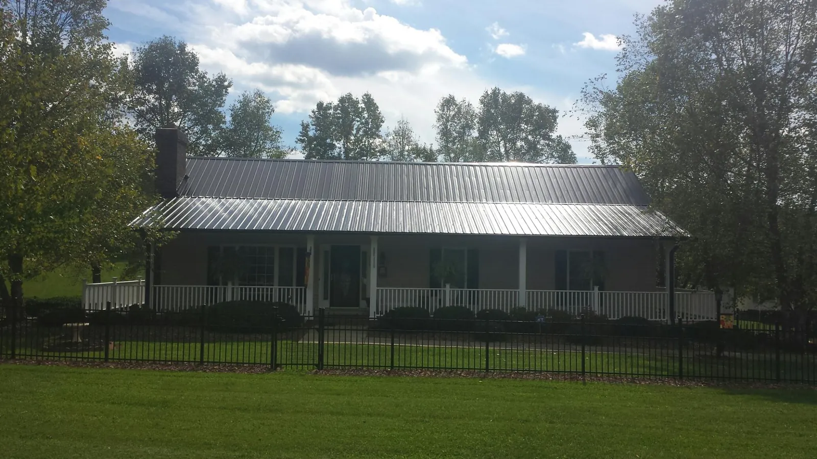 Gray metal roof on a brick ranch with a full width front porch — Gutter Guard Installation work by our crew in Six Lakes