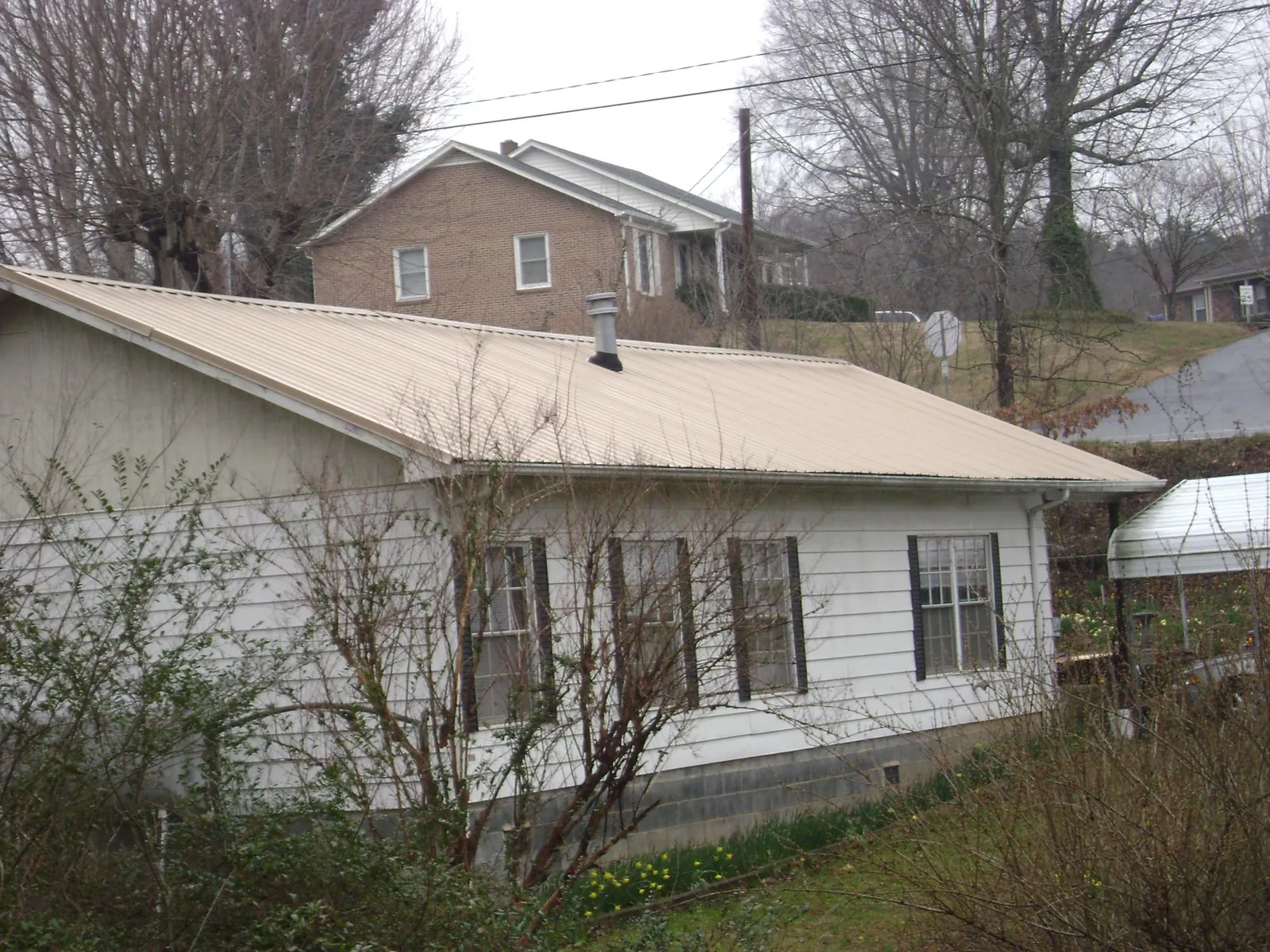 Tan metal roof on a white sided house set into a hillside — Commercial Roofing by Roofing Brothers in Six Lakes