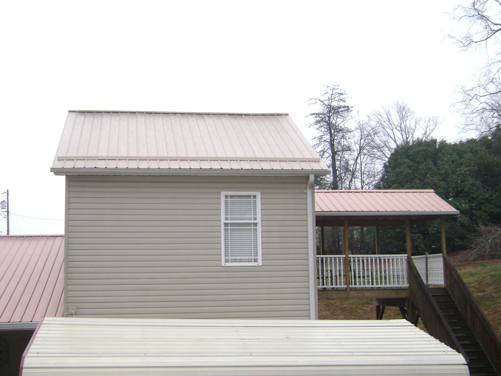 Tan metal roofs on a two story addition and attached porch, from a Roof Replacement job in Six Lakes